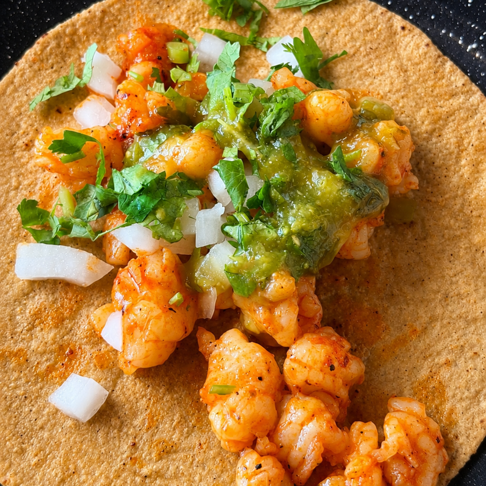 Shrimp taco on a crisp tortilla, topped with green salsa, chopped onions, cilantro, and jalapeño.